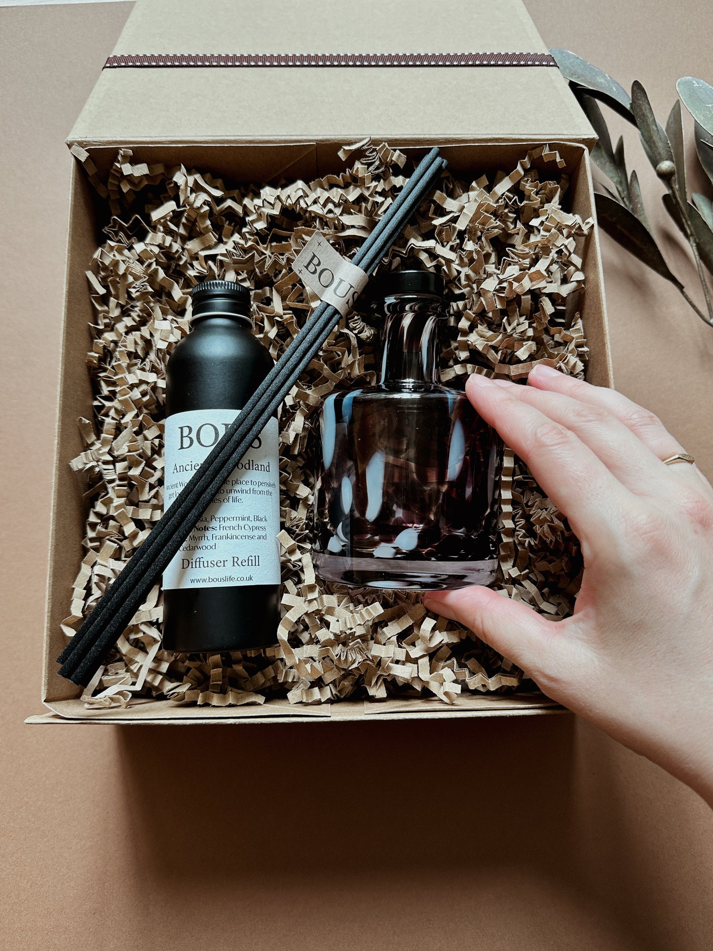 Bous Diffuser set with bottles and reeds in a box, hand reaching to touch one of the bottles.