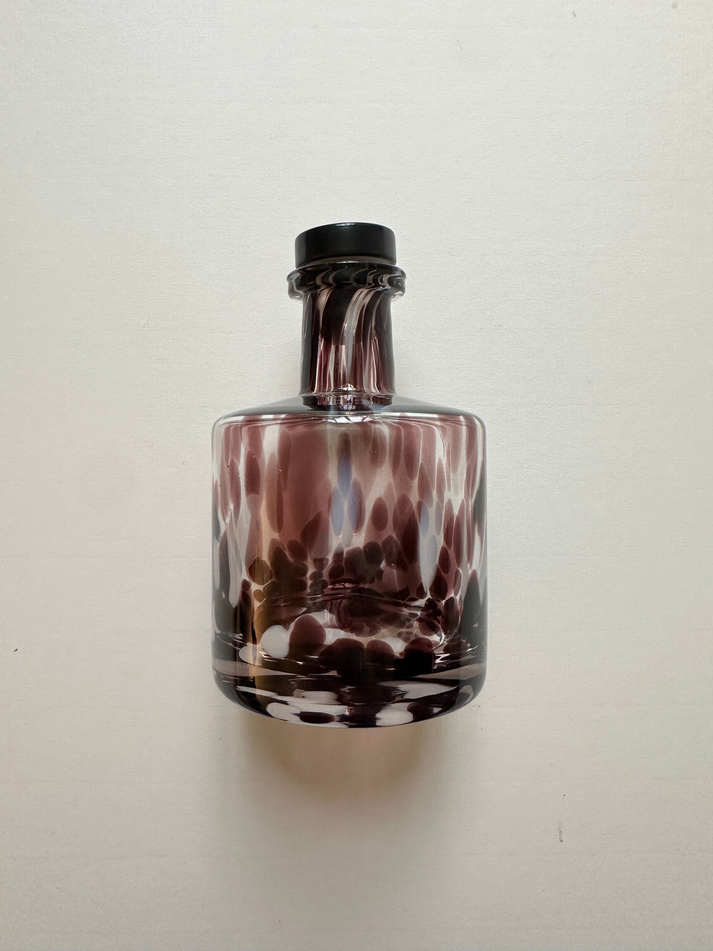 Glass bottle with a wine coloured spotted design on a white background