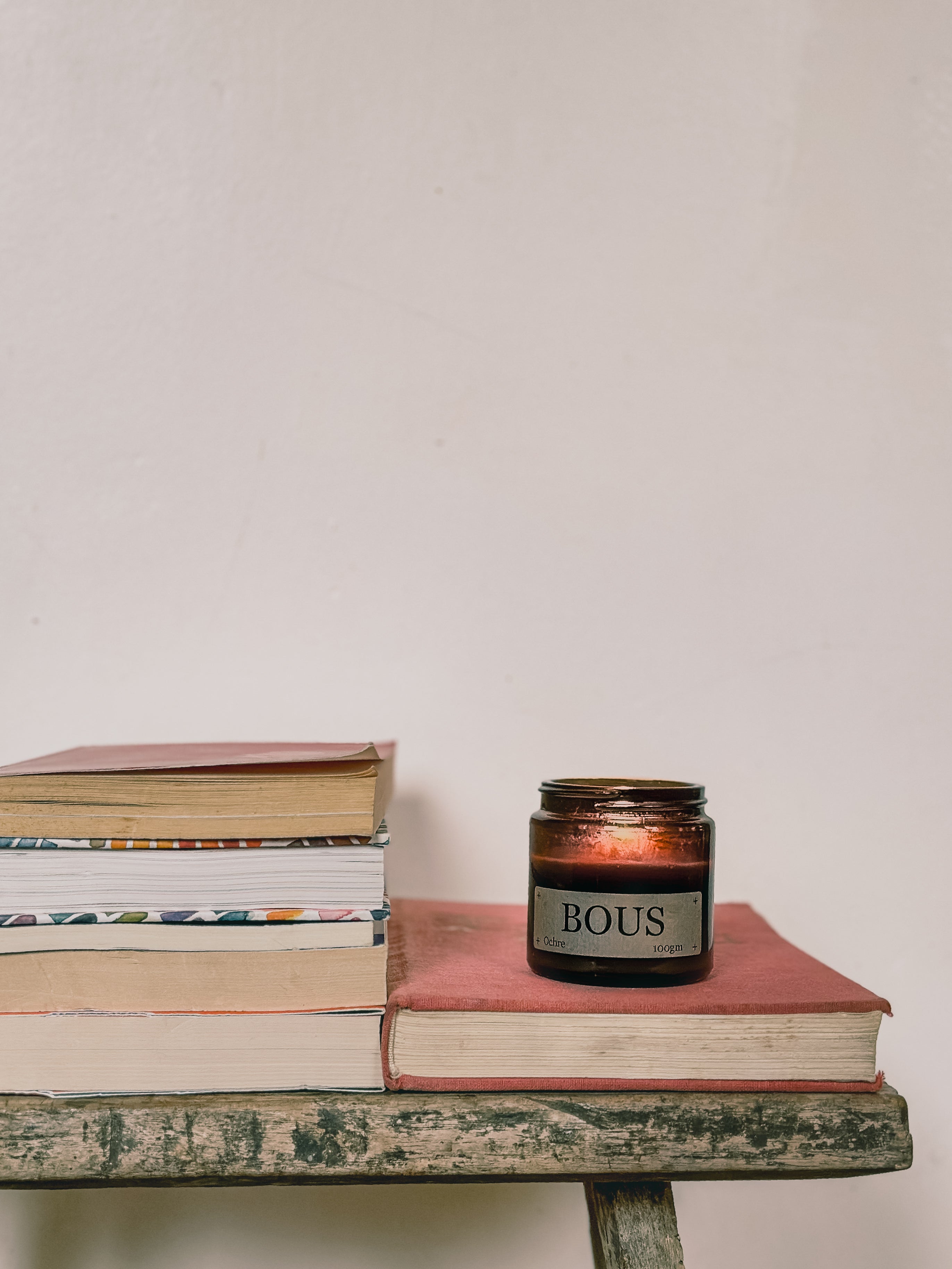 Candle labeled 'BOUS' on a stack of books with a plain background